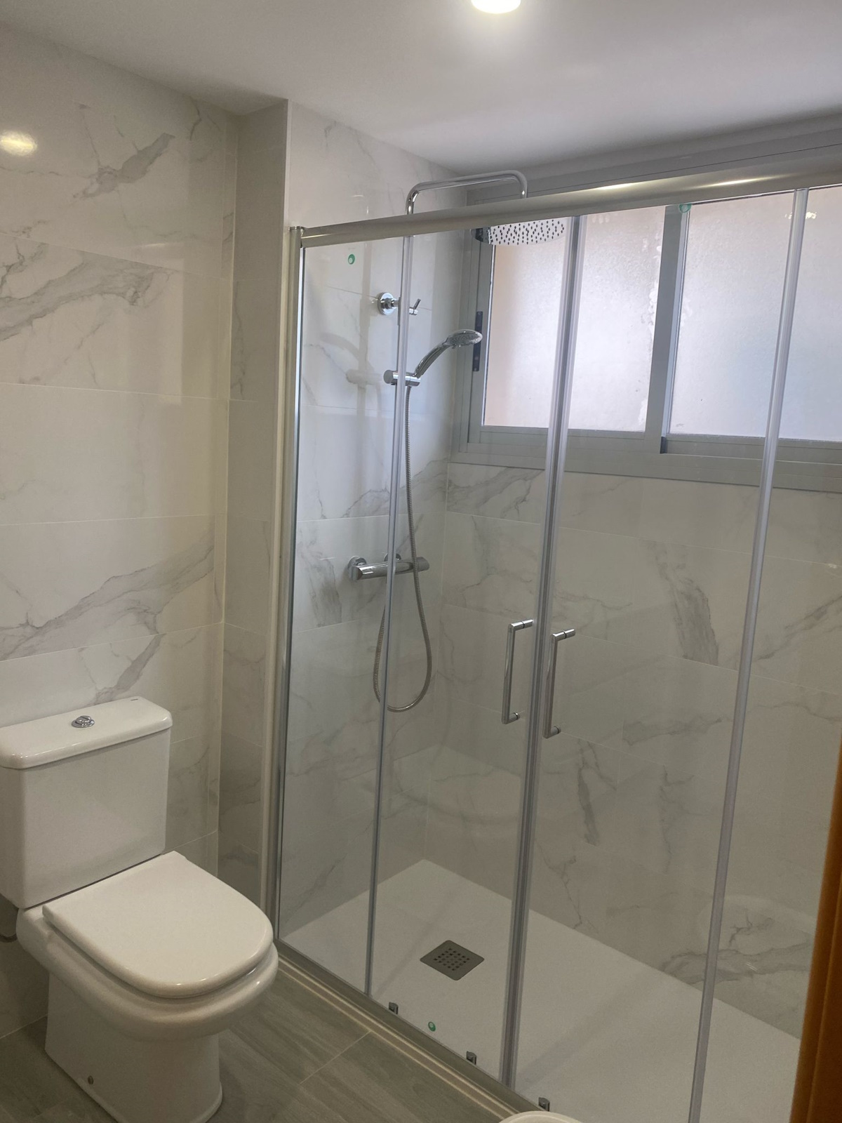 Baño reformado con nuevos azulejos y ducha a nivel de suelo para mayor accesibilidad.